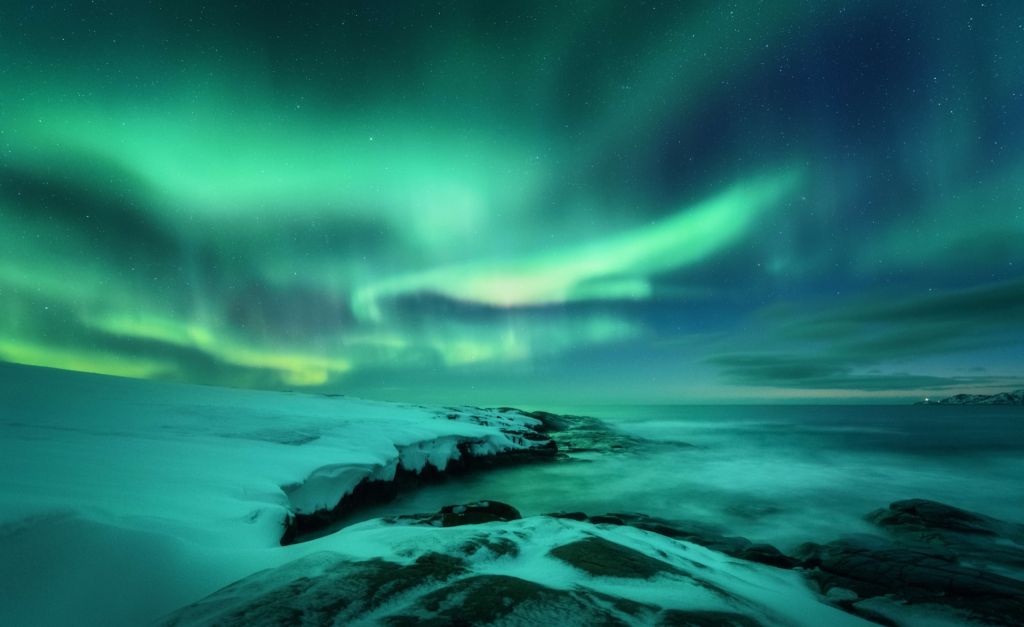 Groen noorderlicht boven besneeuwde rotsen